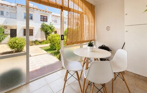 Ein Balkon mit weißem Tisch und Stühlen, einem Blumentopf und Blick auf einen Innenhof mit Gebäuden.