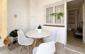 Un coin repas avec une table ronde, quatre chaises blanches, une petite plante en pot et un barbecue.