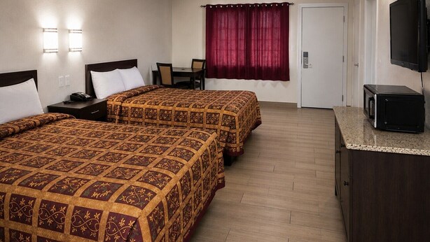 A hotel room with two beds, a desk, a chair, a television, and a door.