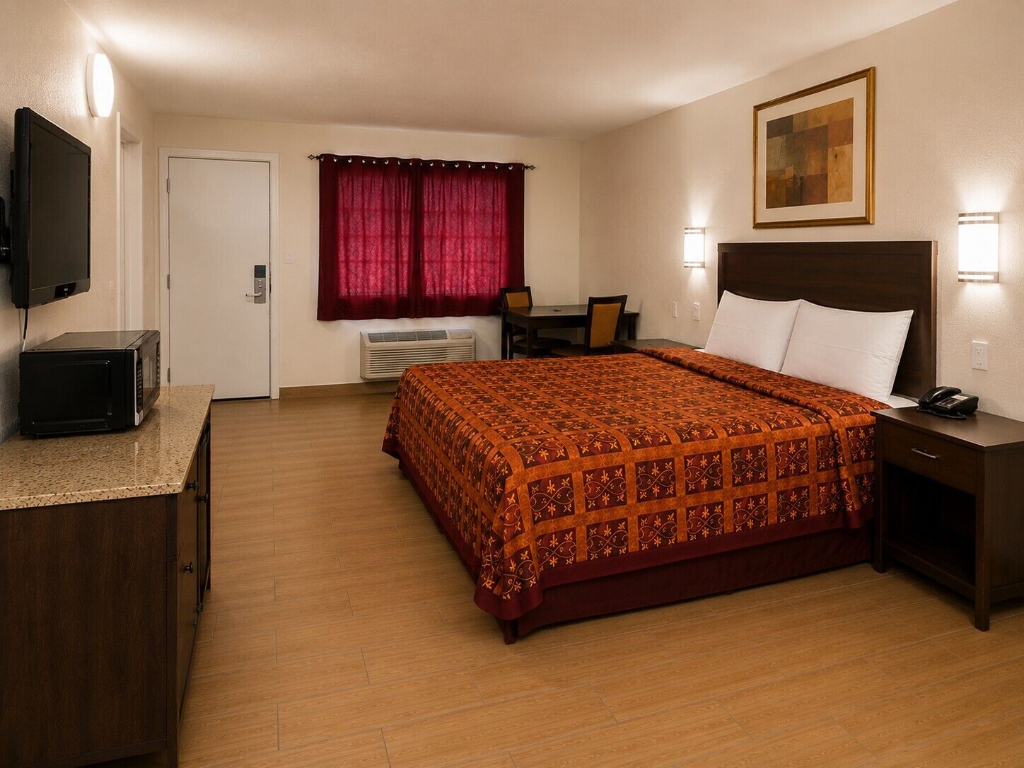 Una camera d'albergo con un letto, comodino, scrivania, sedia, televisore e un quadro appeso al muro.