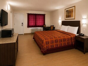 Habitación de hotel con cama, mesita de noche, escritorio, silla, televisor y un cuadro en la pared.