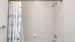 A bathroom with a shower curtain, a bathtub, and a showerhead.
