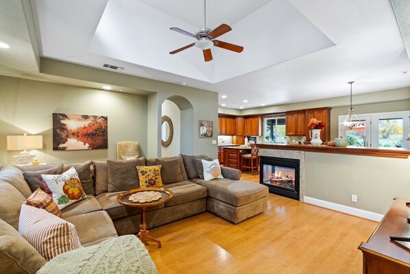 A spacious living room with a sectional sofa, a fireplace, and a ceiling fan.