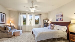 Quarto com cama, sofá, ventoinha no teto, mesa de cabeceira e janela com cortinas.