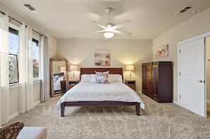 A bedroom with a bed, a ceiling fan, a dresser, and a door.