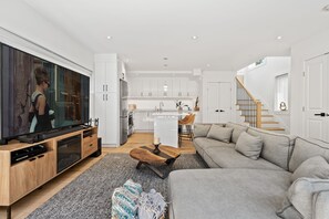 Ein modernes Wohnzimmer mit einem großen Flachbildfernseher, einem grauen Sofa und einem Holztisch.