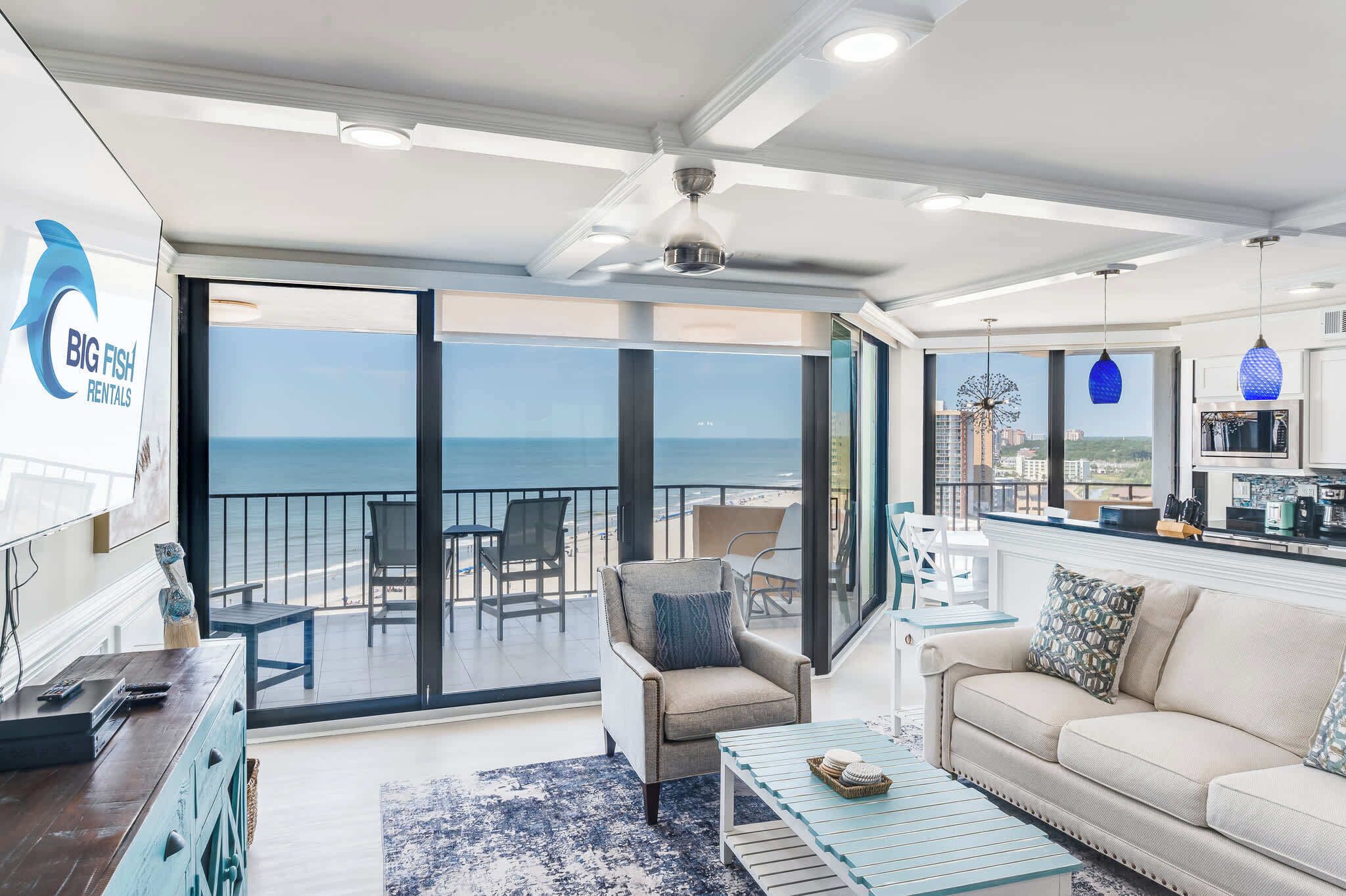 Un vaste espace de vie avec un balcon donnant sur la mer, une kitchenette et un coin salon comprenant un canapé et des fauteuils.
