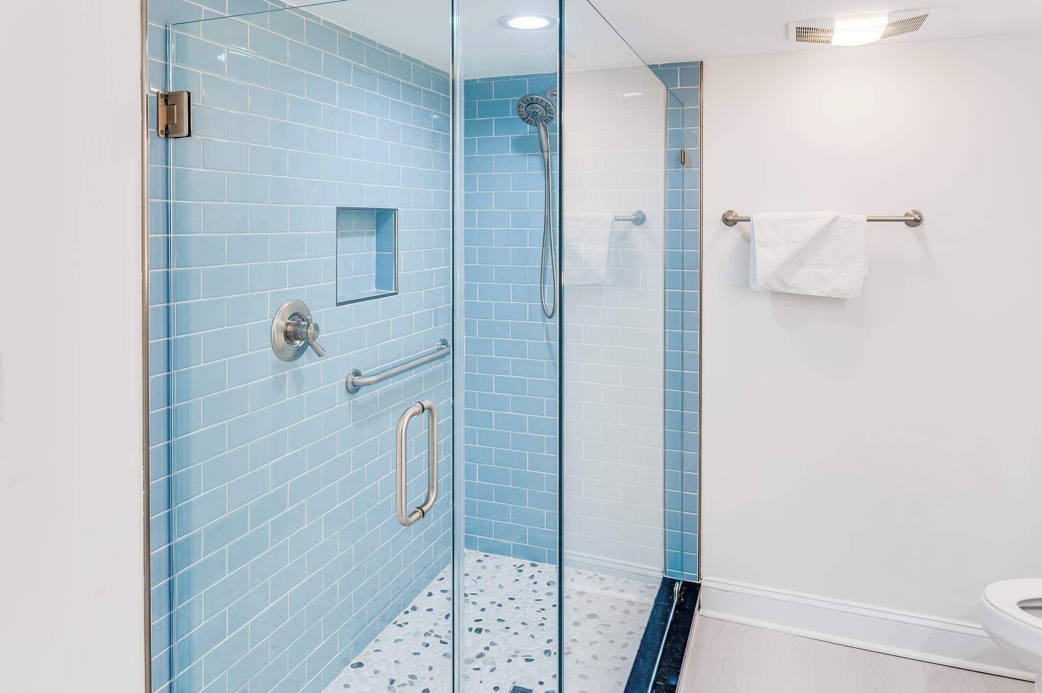A glass-enclosed shower with a handheld showerhead and a handheld shower control.