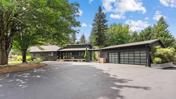Ein zweigeschossiges Haus mit Garage, Auffahrt und umliegenden Bäumen.