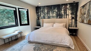 Ein Schlafzimmer mit einem großen Bett, einer Bank, einem Fenster und einer Wandmalerei zum Thema Wald.