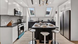 A modern kitchen with a central island, a dining area, and a view through the skylight.