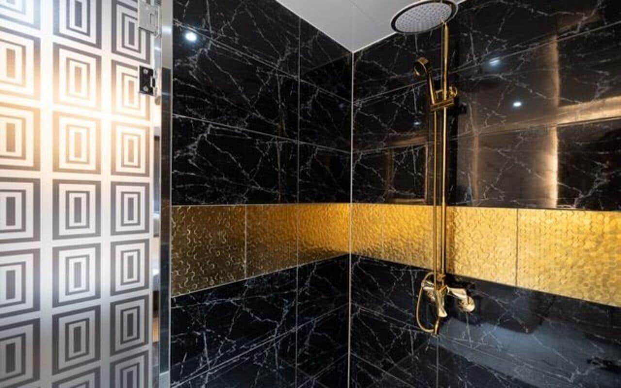 A bathroom with black marble walls, a gold accent wall, and a shower with a golden fixture.