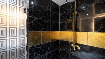 A bathroom with black marble walls, a gold accent wall, and a shower with a golden fixture.