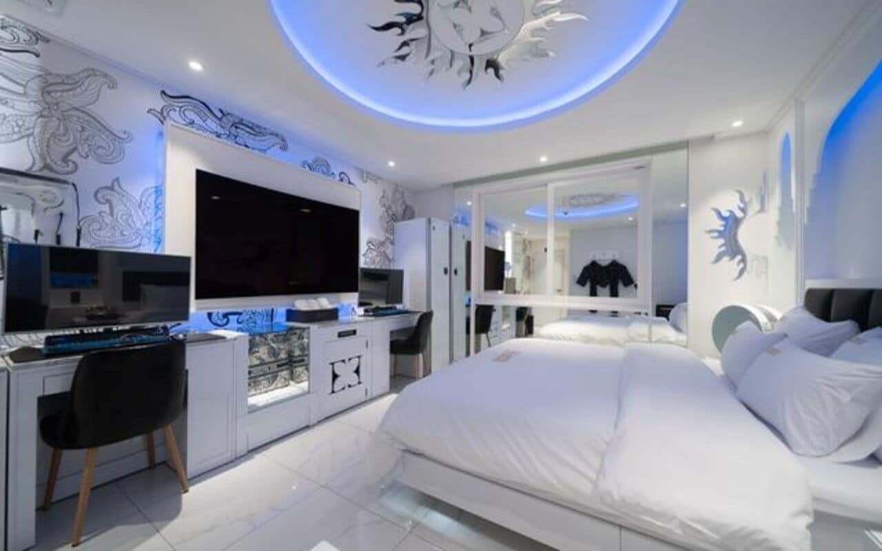 Un dormitorio moderno con una cama grande, un escritorio con una computadora y una televisión.