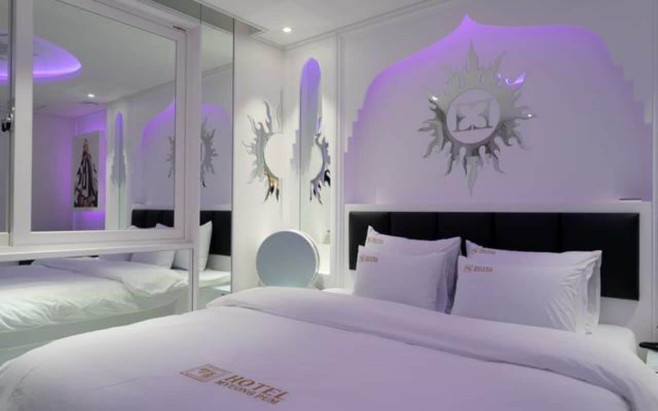 A hotel room with a large bed, a round mirror, and decorative wall art.