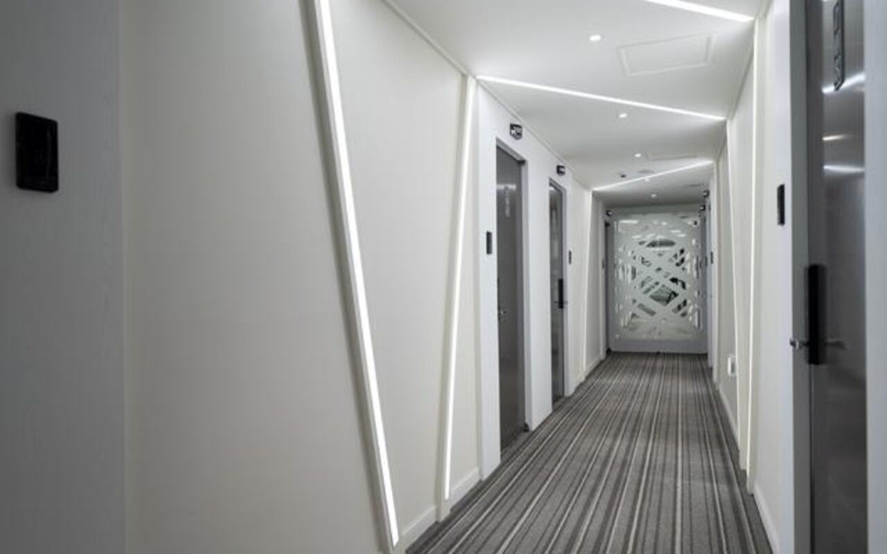 Corredor moderno de hotel com caminho reto, portas e carpete estampado.
