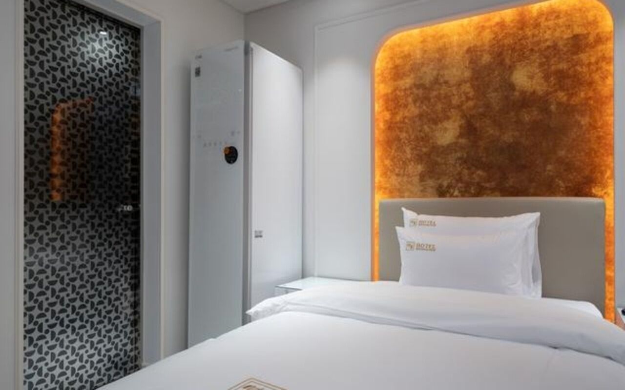 Ein Hotelzimmer mit Bett, Kopfteil, Kleiderschrank und einer Wand mit strukturierter Oberfläche.