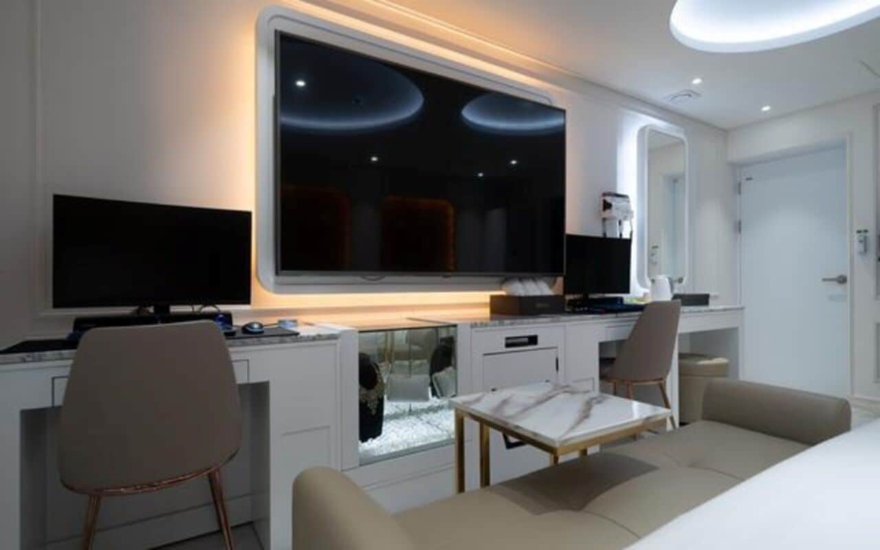 Et moderne hotelværelse med et stort fladskærms-tv, et skrivebord med computer, en behagelig sofa og et lille bord.
