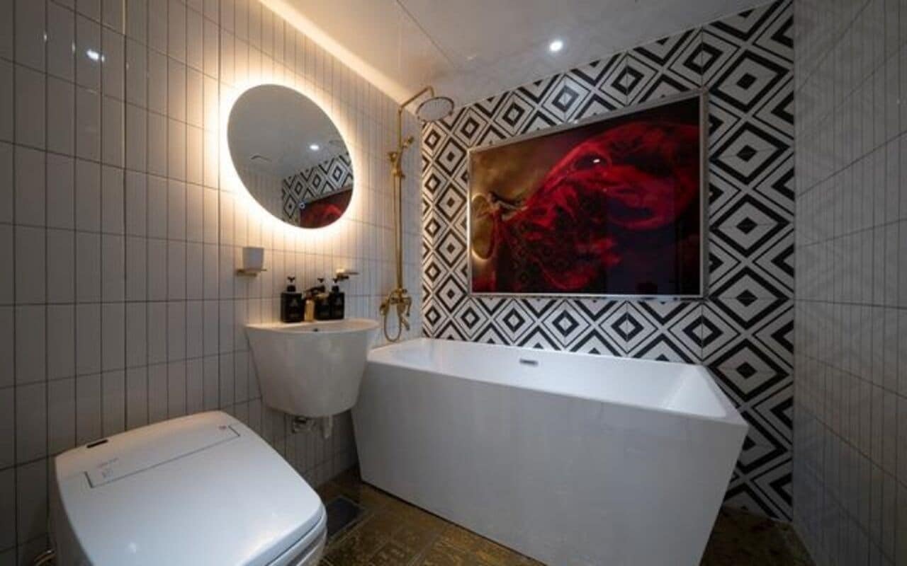 Une salle de bain moderne avec des toilettes blanches, une baignoire sur pieds, un miroir rond et un lavabo fixé au mur.
