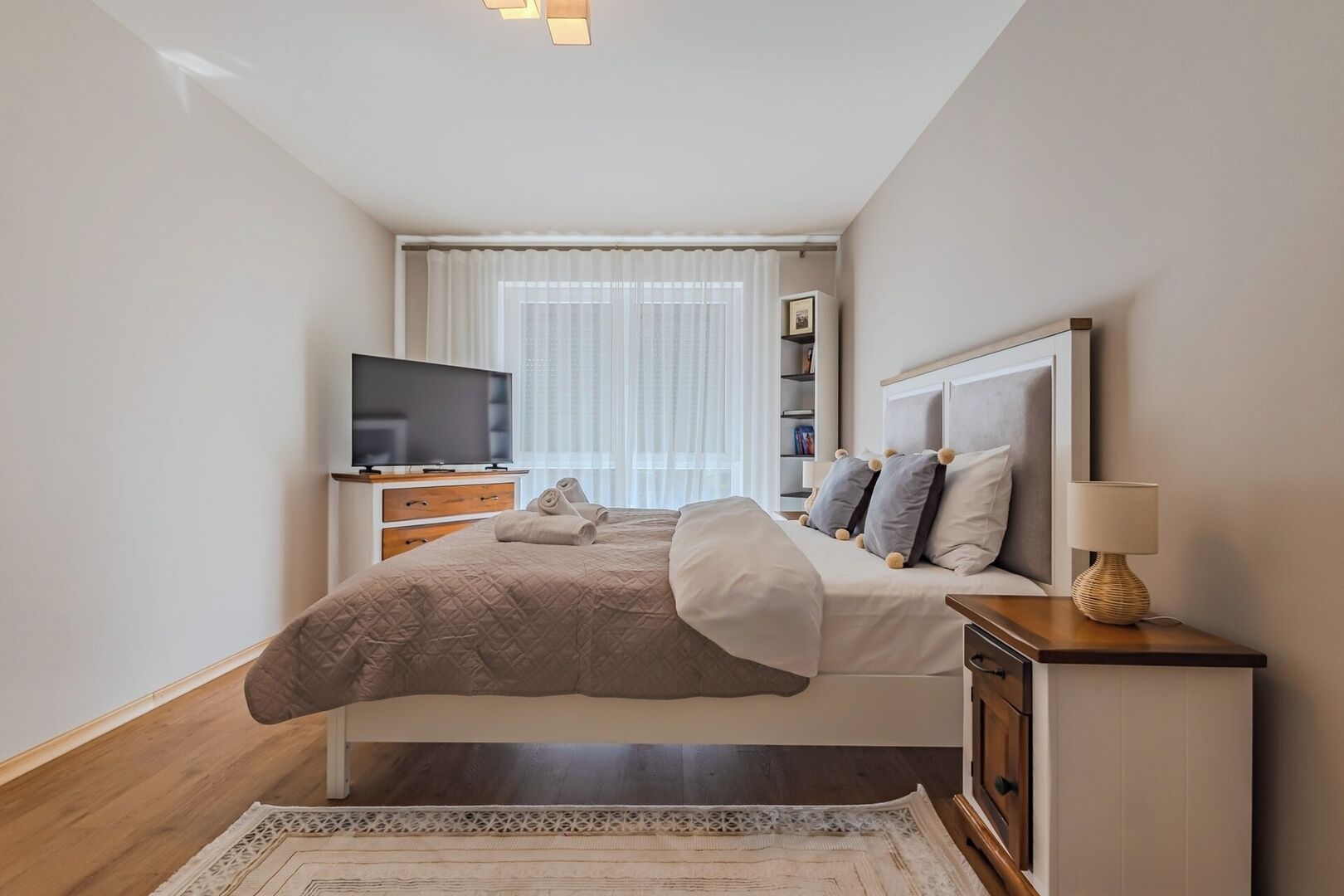 A hotel room with a bed, a television, a bedside table with a lamp, and a window with curtains.