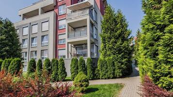 A multi-story residential building with balconies, surrounded by well-maintained greenery and a paved pathway.