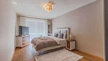 A modern bedroom with a bed, bedside tables, a TV, and a window with curtains.