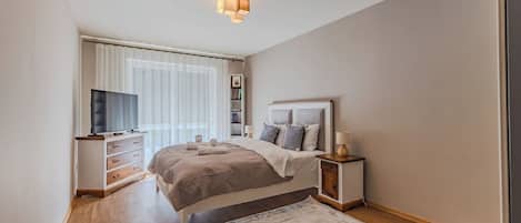 A modern bedroom with a bed, bedside tables, a TV, and a window with curtains.