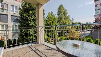 A balcony with a glass table, metal railing, and a view of a residential area with trees and buildings.