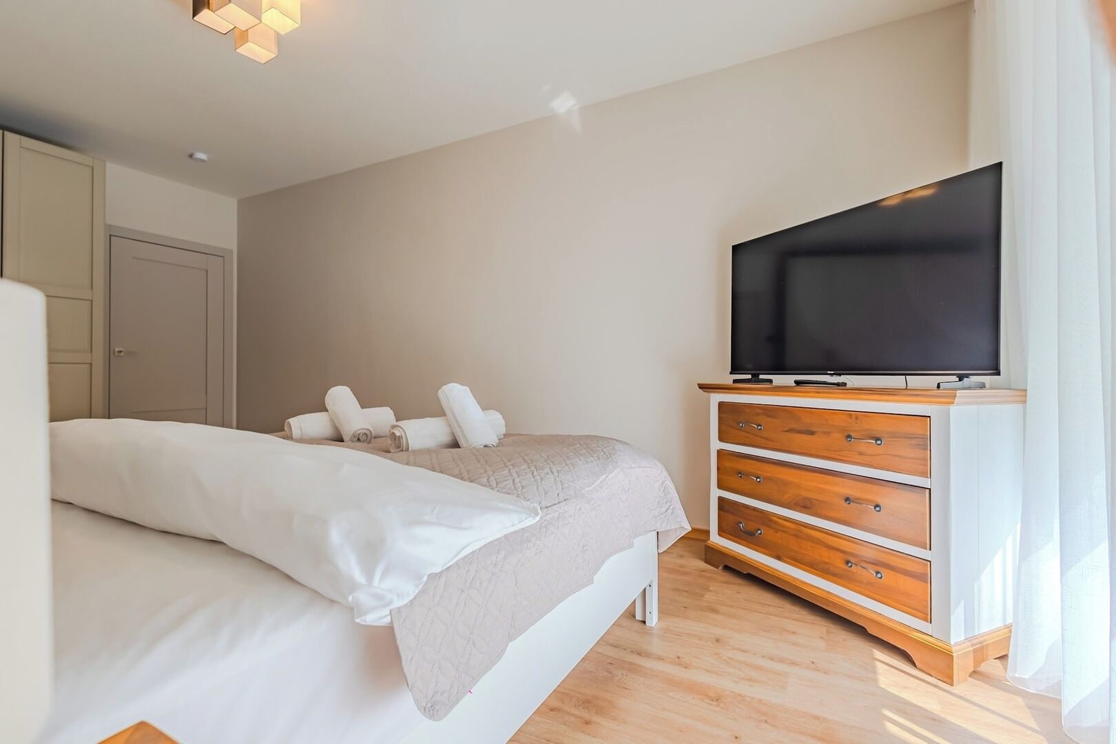 A bedroom with a bed, a TV on a wooden dresser, and a wardrobe.