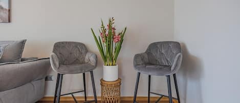 Una sala de estar moderna con un sofá gris, dos sillones grises, un jarrón blanco con flores rosadas y una mesita lateral tejida.