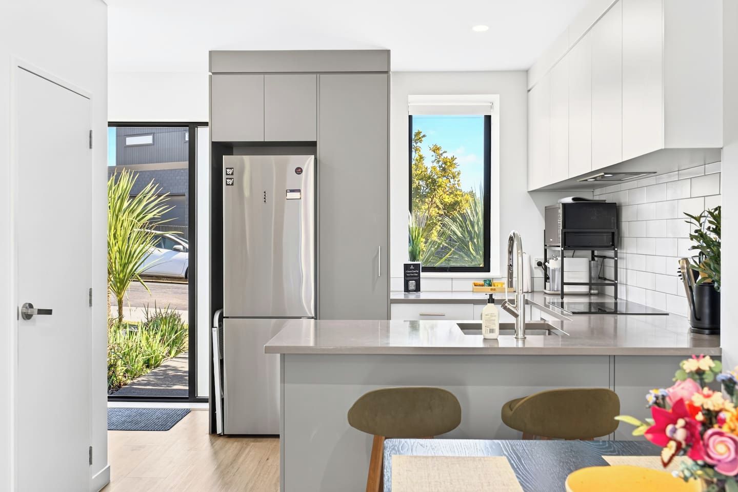 A modern kitchen with a built-in refrigerator, a sink, and a window with a view of trees.