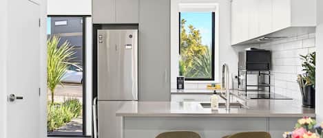 A modern kitchen with a built-in refrigerator, a sink, and a window with a view of trees.