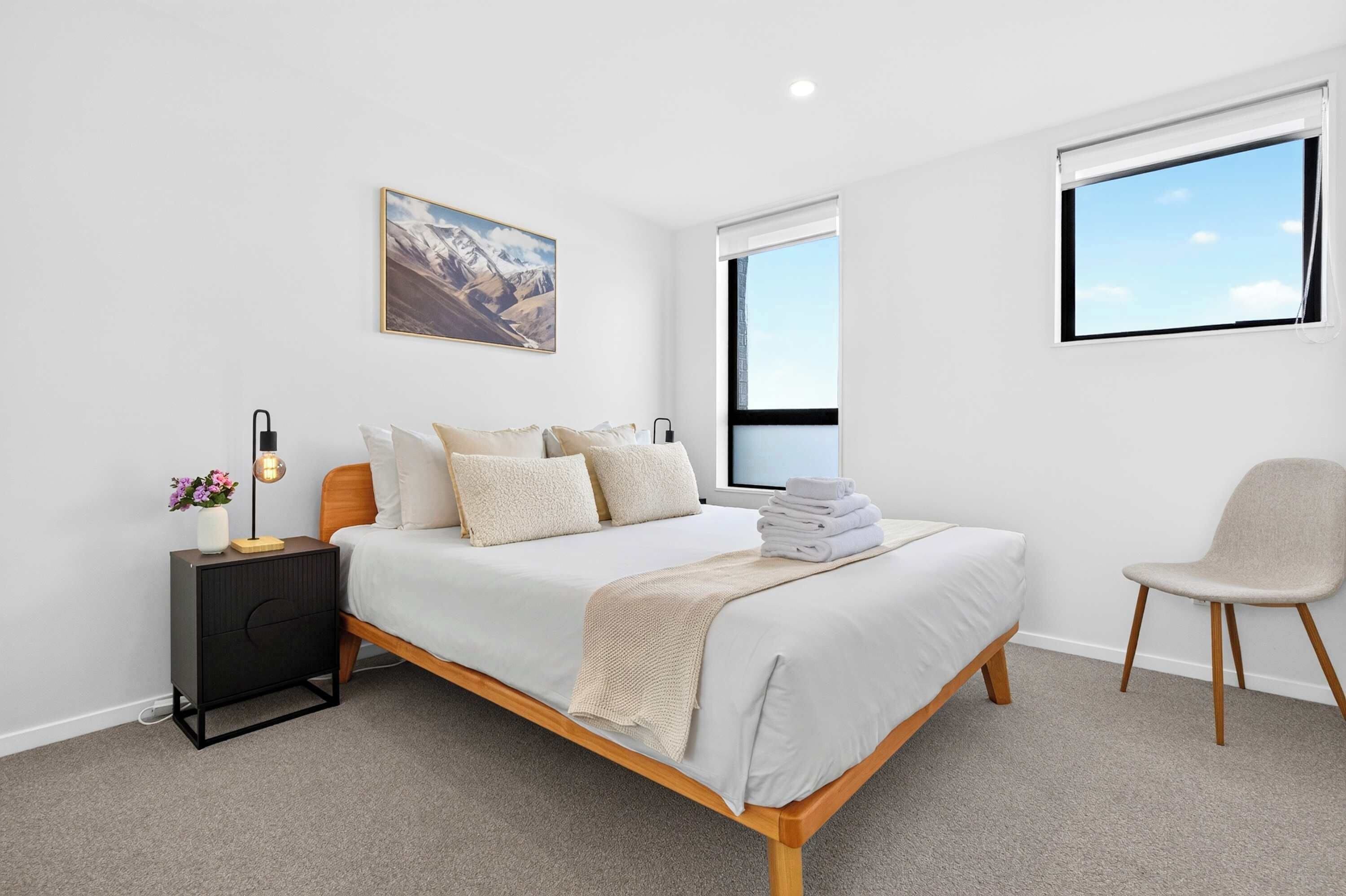 A modern bedroom with a bed, bedside table, lamp, and a chair.