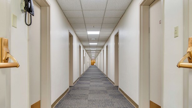 Ein langer, schmaler Hotelgang mit Teppichböden und weißen Wänden.