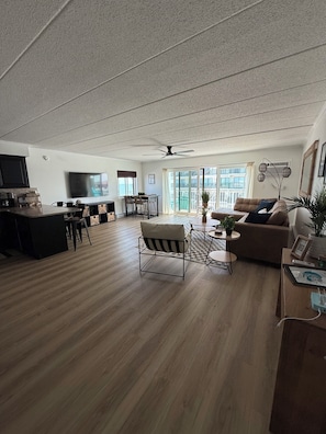 A spacious living area with a wooden floor, a sofa, a dining table, and a television. - Perfect Walkable Midtown Location, Ocean View, Spacious 2 BR 2 Bath Condo (Ocean City)