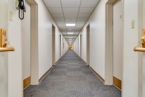 A long, narrow hotel corridor with doors on both sides, carpeted flooring, and a ceiling with fluorescent lighting. - Historic Converted Dorm Room off Vanderbilt! (Nashville)