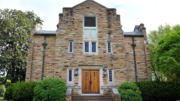 Un bâtiment en pierre avec une porte en bois au centre, deux fenêtres de chaque côté et un petit escalier menant à l’entrée.