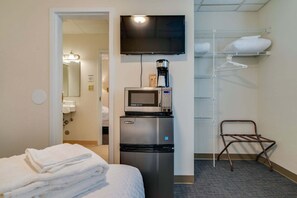 A hotel room with a bed, a TV, a coffee maker, a microwave, a shelf with towels, and a chair. - GREAT Location! Historic Suite! Budget Friendly!! (Nashville)
