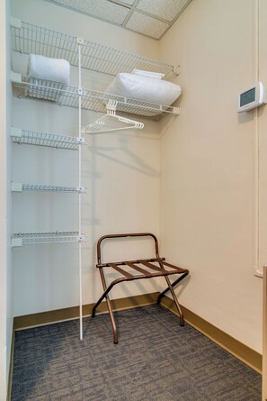 Ein Teil eines Hotelzimmers mit einem Wäschegestell, einem Stuhl und einem Thermostat an der Wand.