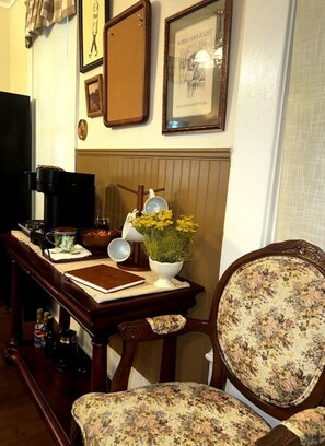 A room with a wooden table, a chair with floral upholstery, a framed picture of 'Romeo and Juliet', and a coffee maker.
