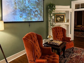 A room with two armchairs, a chessboard, a painting, and a fireplace.