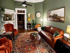 A living room with a brown leather sofa, a patterned rug, a chessboard, and a wall clock.