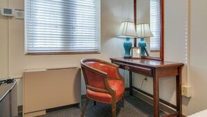 A hotel room with a wooden desk, a chair, a lamp, a mirror, and a window with blinds. - Converted Suite! AMAZING LOCATION! (Nashville)