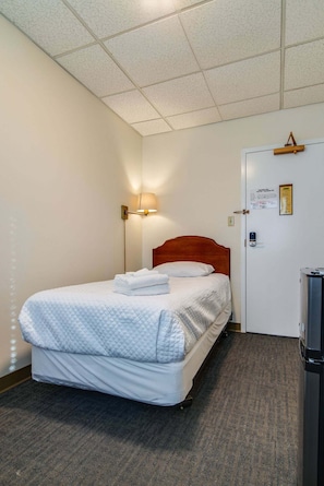A hotel room with a bed, a nightstand, a lamp, a door, and a trash can. - Scarritt Bennett Revamped Dorm Room in Music Row!! (Nashville)