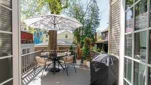 An outdoor patio with a table and chairs, a covered grill, and a large umbrella.