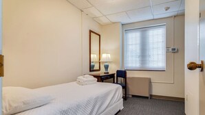 A hotel room with a bed, a desk with a lamp, a chair, and a window with blinds. - AWESOME Location!! Budget Friendly Historic Suite! (Nashville)