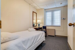 A hotel room with a bed, a desk with a lamp, a chair, and a window with blinds. - AWESOME Location!! Budget Friendly Historic Suite! (Nashville)