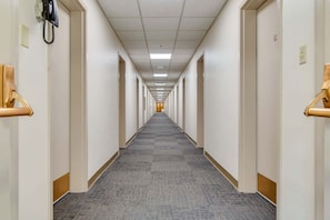 Ein langer, schmaler Hotelgang mit Türen auf beiden Seiten, Teppichboden und einer Decke mit Leuchtstofflampen.