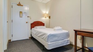 Et hotelværelse med en enkelt seng, et sengebord, en lampe og en dør med et skilt.