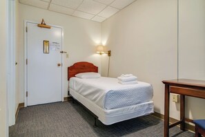 A hotel room with a single bed, a bedside table, a lamp, and a door with a sign. - Converted Dorm in Historic Scarritt Bennett!! (Nashville)